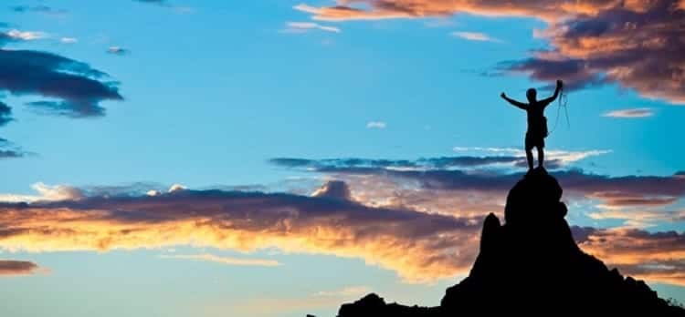 ambition image - silhouete of person on mountain top, with blue sky sunset behind