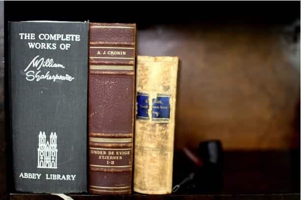 Three old looking books standing upright on a shelf, including the complete works of Shakespeare